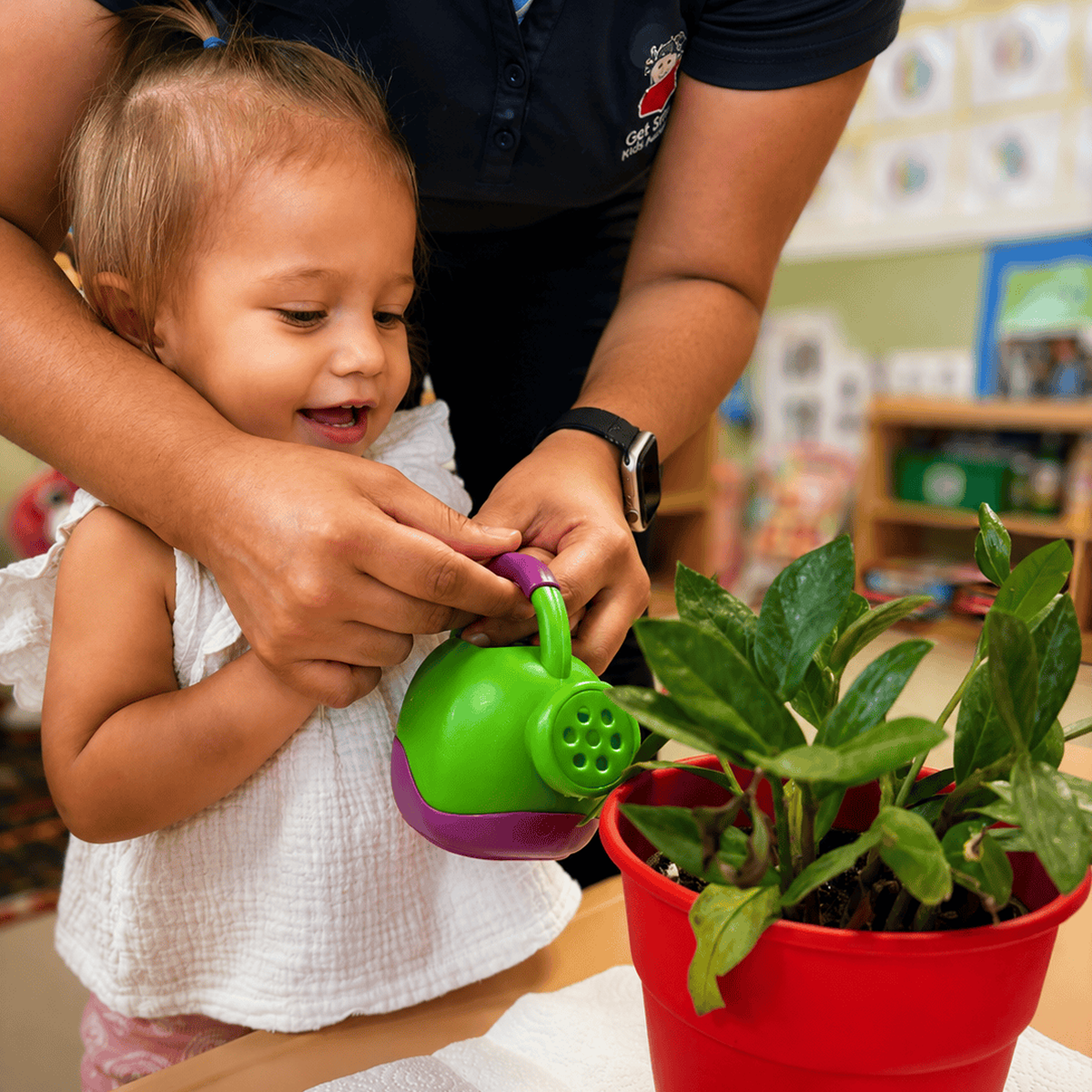 Child watering plant with adult assistance.