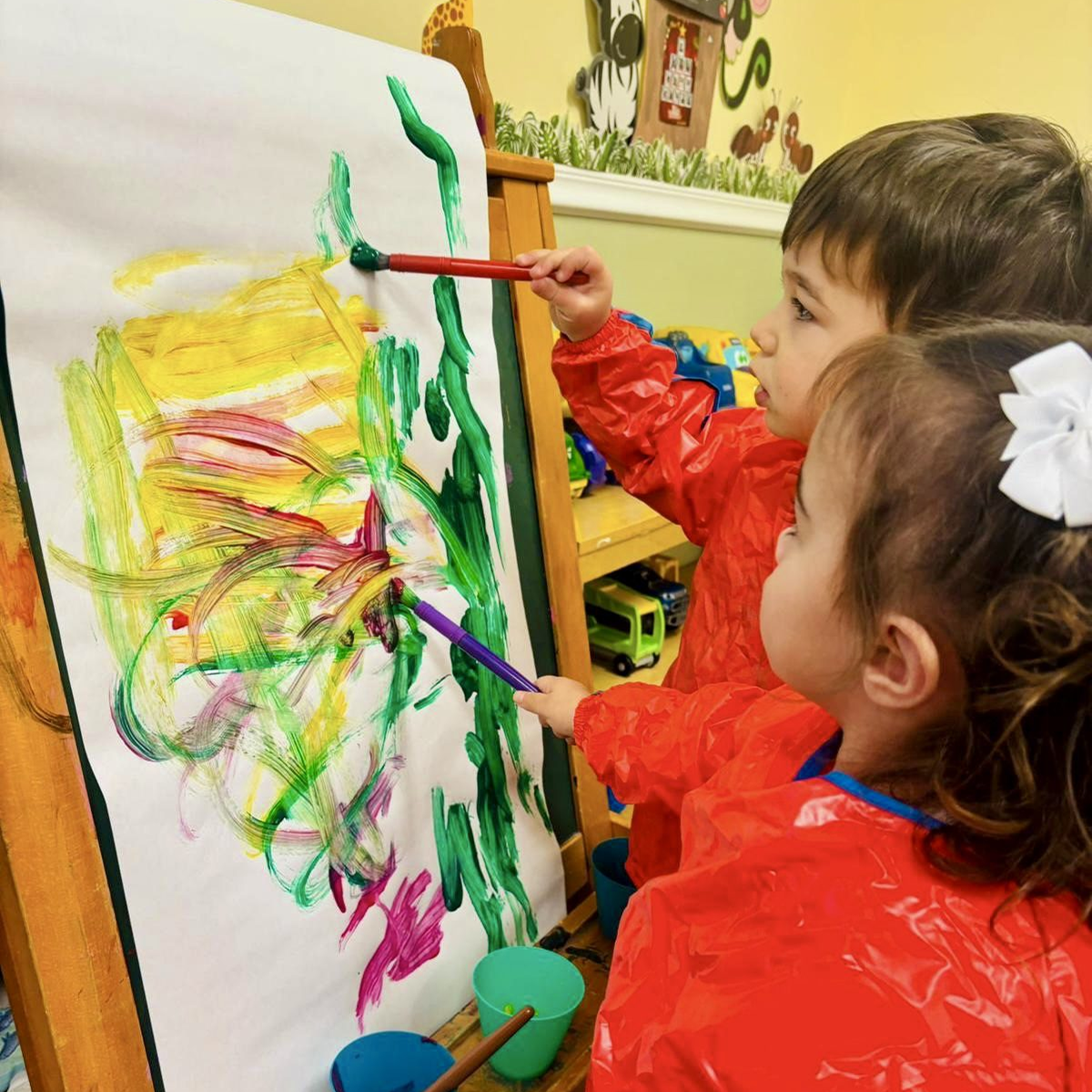 Children painting colorful artwork on easel.