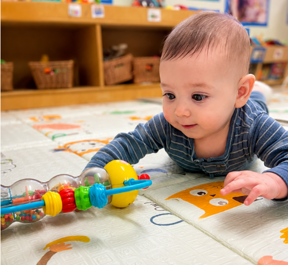 Baby playing with colorful toy on mat.