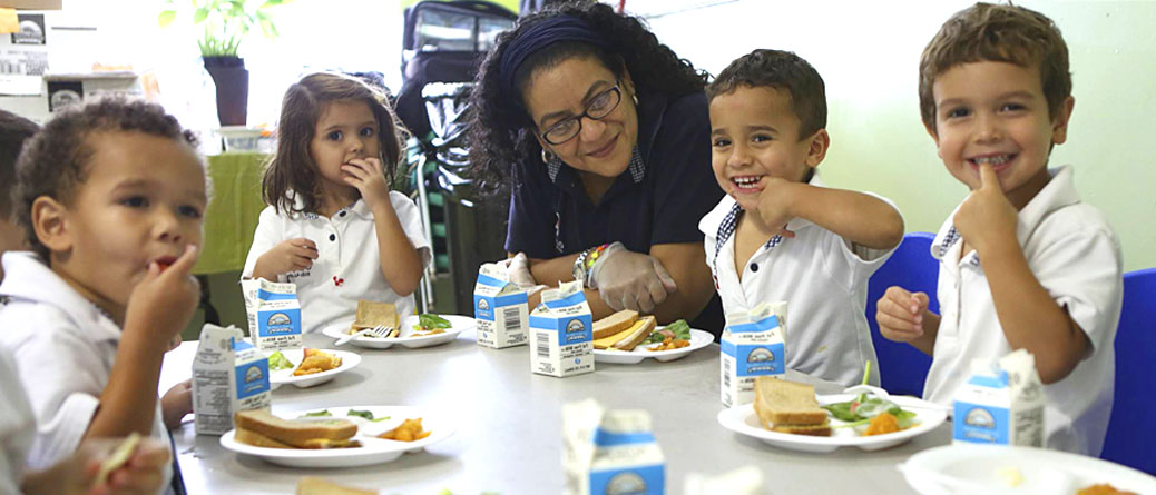 A woman and two children eating sandwiches at the table.