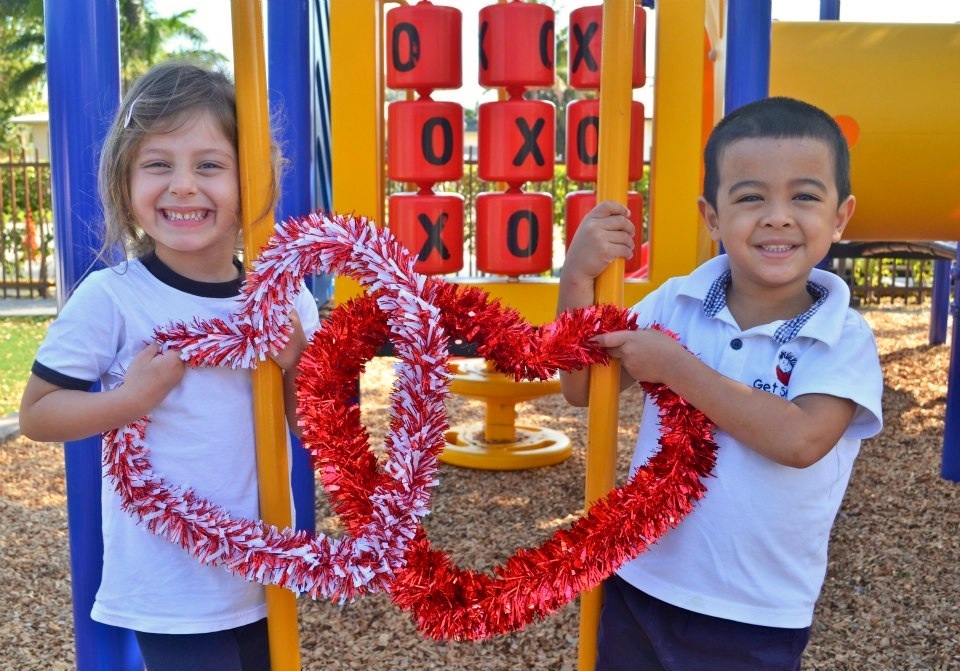 Two children holding a heart shaped wreath in the shape of xo.