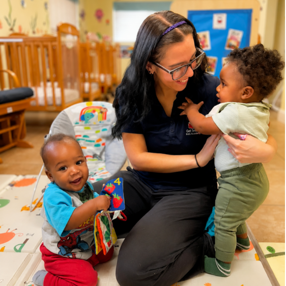 Woman with two smiling toddlers at daycare.